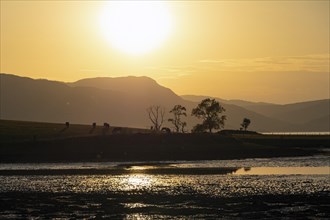 A stunning Scottish sunset over a tranquil landscape of mountains, trees and a loch bathed in