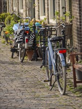 Bicycles parked in a quiet, cobbled street in the old town, historic houses in Hoorn and ships in