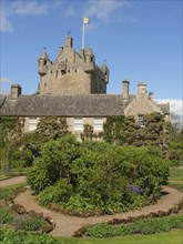 Medieval castle with towers and manicured garden under a blue sky, old grey stone building in a