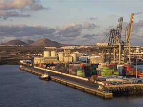 An industrial harbour with container ships and cranes, in the background mountains and clouds in