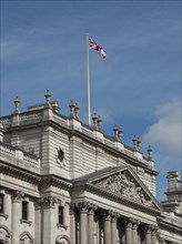 Historic building with a waving Union Jack flag on the roof, against a blue sky, London, England,