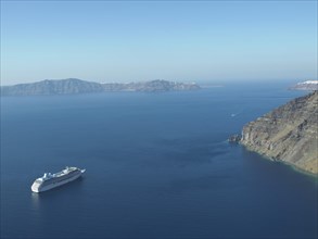 A cruise ship sails in the calm blue sea near a rocky coast under a clear sky, The volcanic island