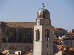 An important bell tower rises above the tiled roofs of a medieval town, the old town of Dubrovnik