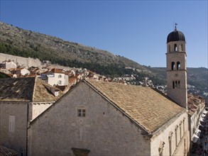 Historic town with church tower and houses in front of a mountain landscape under a blue sky, the
