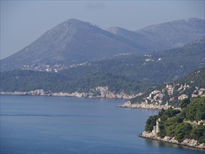 Coastal landscape with mountains, green foliage and calm sea under a clear blue sky, the old town