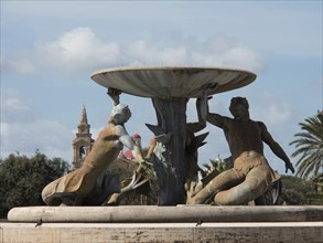 Two statues holding a fountain in an ornate park under a bright blue sky, Valetta, Malta, Europe