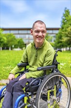Close-up portrait of a happy disabled man in the university campus sitting in wheelchair smiling at