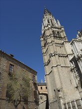 Towering spire of a gothic cathedral, surrounded by historic buildings, under a clear sky, toledo,