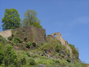 Stone ruins on a hill with green trees and blue sky in the background, old castle ruins over a