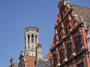Historic buildings in Bruges with a high tower and colourfully decorated facades on a clear day,