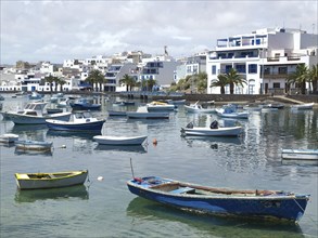 Fishing boats moored in the quiet harbour, surrounded by white buildings and palm trees under a