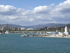 Coastal town with harbour and yachts, surrounded by mountains and slightly cloudy sky, Malaga on