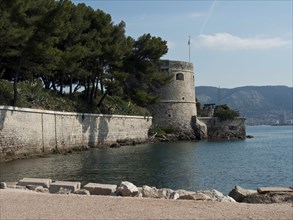 Historic fortress and stone wall on the coast, surrounded by blue water and wooded hills, la seyne