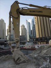 Construction site with an excavator in the foreground and skyscrapers in the background, Dubai,