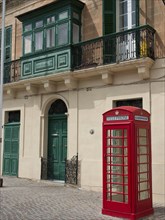Red telephone box in front of a building with green shutters and decorative balconies, Valetta,