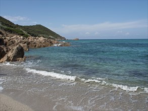 Beach with rocks, gentle waves and clear blue water under a sunny sky, Corsica, Ajaccio, France,