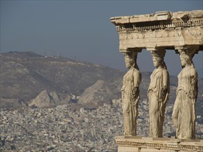 Ancient caryatid sculptures overlooking a city and mountain landscape, ancient columns against a
