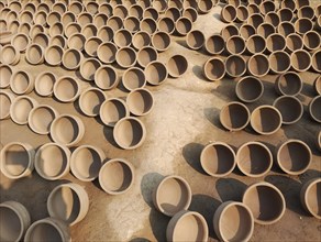 Rows of sunlit clay pots drying on the ground in an organized manner