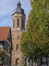 Church tower and half-timbered houses, surrounded by autumnal trees, under a blue sky, historic