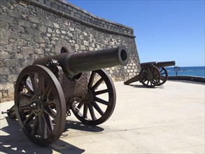 Two ancient cannons next to a fortress with a view of the sea, the island of Lanzarote with