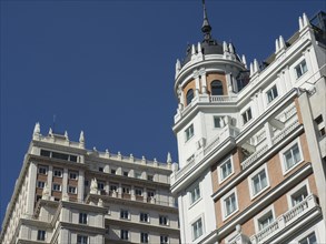 Detail of two tall buildings with different architectural styles, all under a blue sky, Madrid,