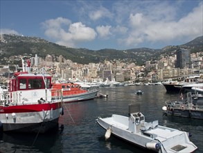 Various boats and yachts in the harbour with a mountainous cityscape in the background under a