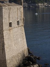 Massive stone walls of a fortress tower over the calm sea with a small boat, the old town of