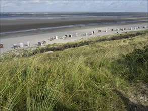 Grassy dunes with view of beach and sea with scattered beach chairs and cloudy sky, Spiekeroog,