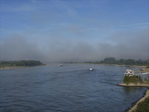 Calm river landscape of the Rhine under a blue sky with several sightings of boats and wooded