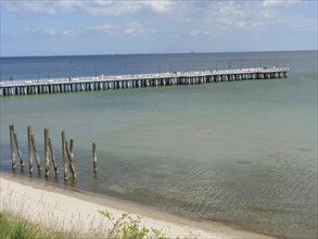 A long jetty leads into the calm sea under a cloudy sky on a sandy beach, spring on the Baltic