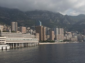 High-rise buildings on the coast against a mountain backdrop under a cloudy sky, monaco on the
