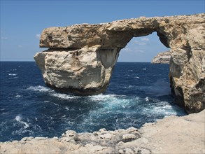 Dramatic rock formation with a natural arch over the blue ocean, under a clear sky and surrounded