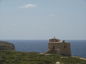 An old watchtower lies on the coast, right next to the deep blue sea, the island of Gozo with