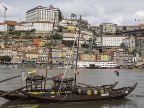 Traditional boats on a river in front of an old town, Portuguese flags and historical atmosphere,