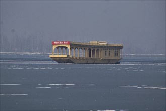 A houseboat named 'New Bul Bul' floating on a calm lake with a serene backdrop