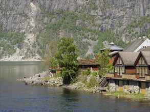 Charming wooden cabins by the water with steep cliffs and green trees in an idyllic mountain
