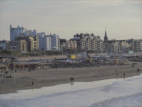 An urban beach setting with a mix of modern and old buildings, some people on the beach and calm