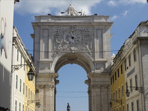 Historic triumphal arch with decorations and sculptures, flanked by yellow buildings, Lisbon,