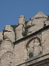 A single stone arch of a ruin in front of overwhelming rocks and blue sky, monastery in rocky