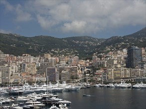 Panorama of harbour and city with many yachts and skyscrapers in front of a mountainous landscape,