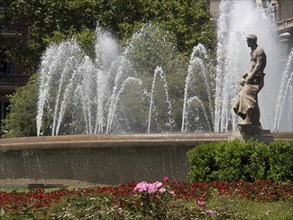 Male statue in a large fountain surrounded by splashing water and colourful flowers, fountain in