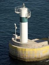 White-green lighthouse in the sea on a concrete base, Ancient building with columns and trees on