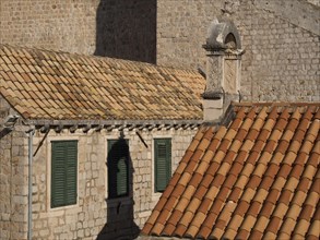 Red tiled roofs and green shutters, with shadows on old stone walls, the old town of Dubrovnik with
