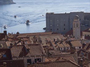 View of the tiled roofs of a coastal town with boats and fortress in the background, the old town