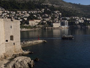 Quiet bay with a historic fortress, boats and buildings on the shore at the foot of the mountains,