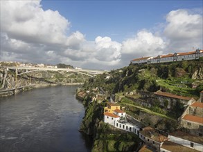 Buildings on rocky cliffs along a river, with a bridge in the background under a clear sky, spring