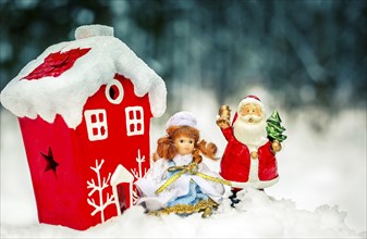 Christmas decorations with a red house and figurines of Santa Claus and a girl doll in a snowy