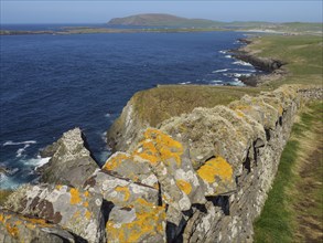 Coastal landscape with a stone wall running along the cliffs, with blue sea and sky, Green meadows