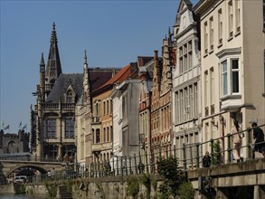 A street along a canal with gothic towers and historic houses under a clear blue sky, medieval