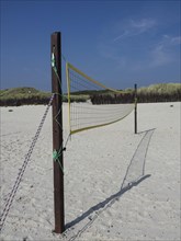 A volleyball net is set up in the sand on the beach, surrounded by dunes and grass, Heligoland,